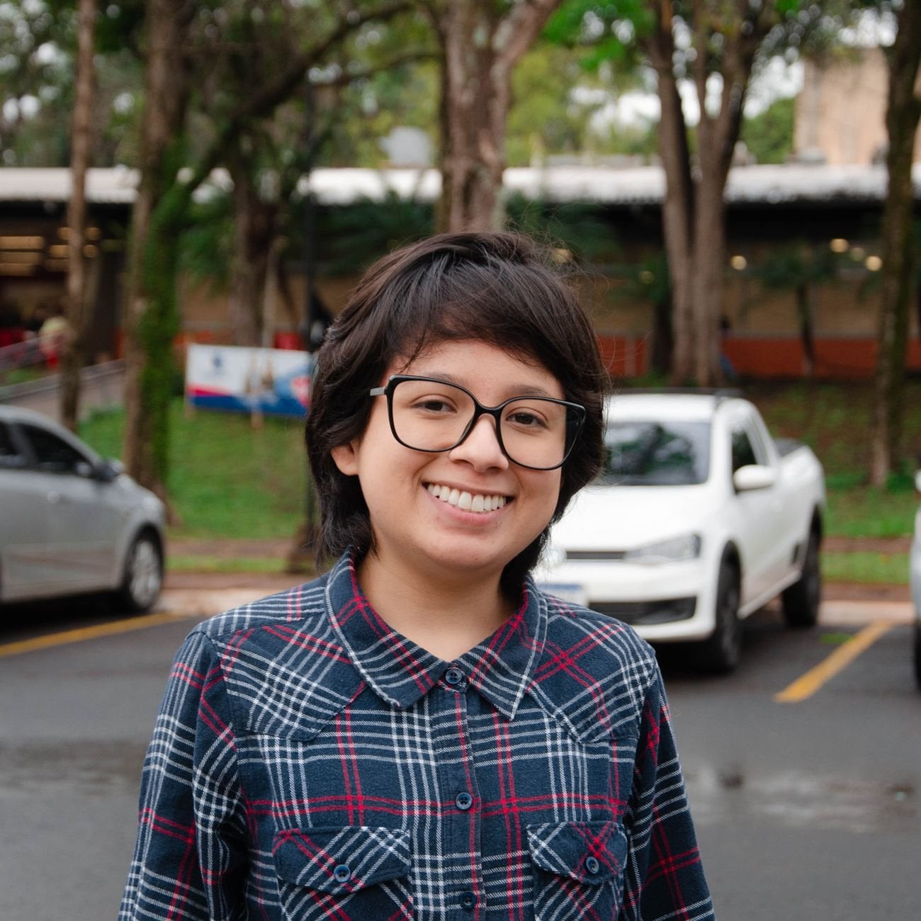Smiling young person with glasses in a casual outdoor urban scene.